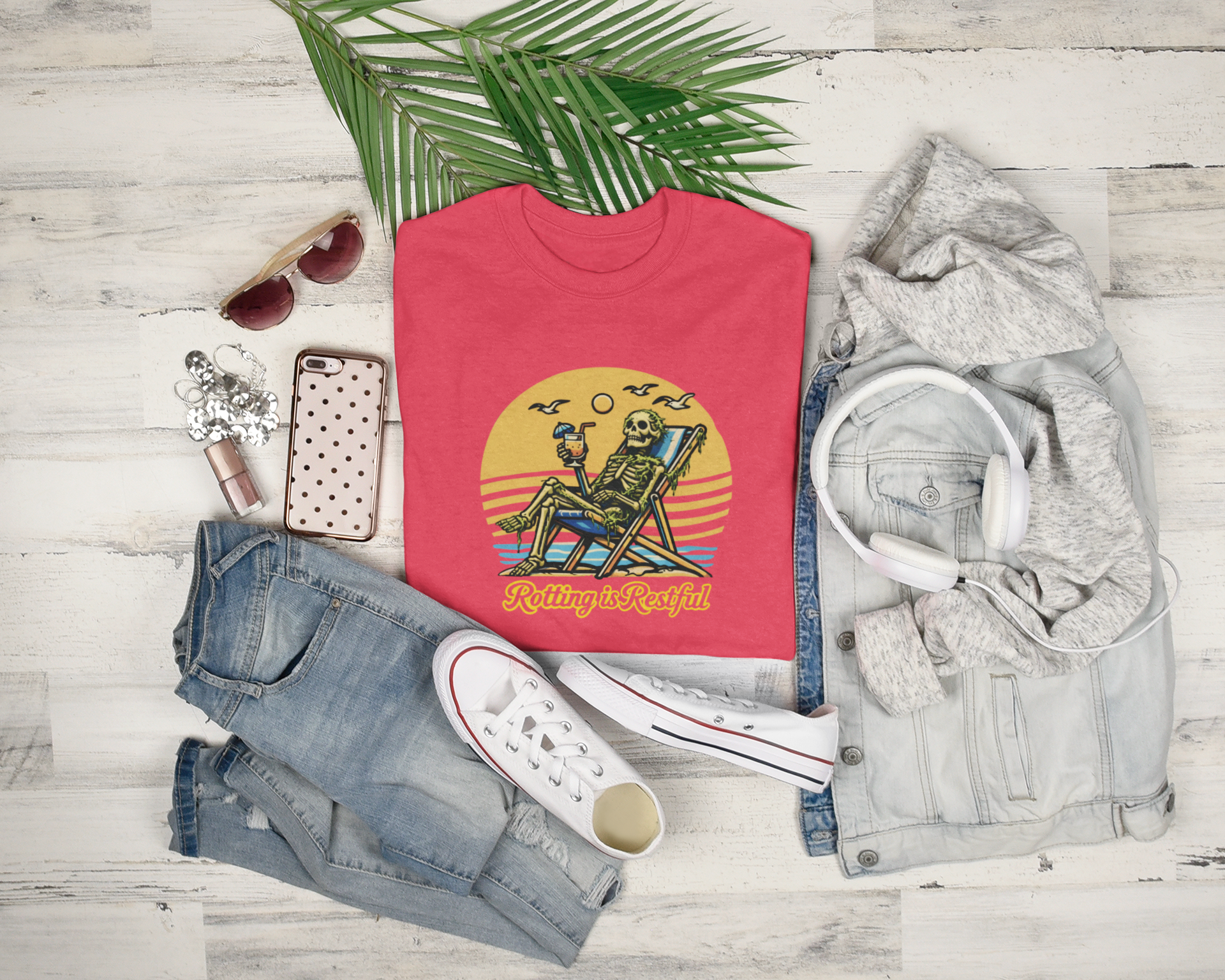 Red t-shirt with skeleton design on a wooden surface with jeans, sneakers, and a jacket. Rotting is Restful tagline. Relax, anti-hustle culture shirt